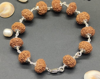 May include: A brown bracelet with silver beads and a pearl charm. The bracelet is made of rudraksha beads, which are believed to have spiritual and healing properties.
