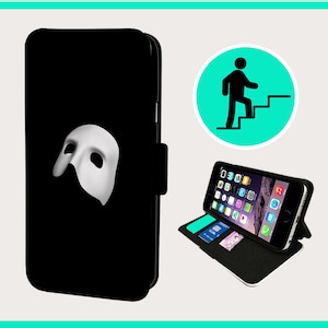 May include: A black phone case with a white Phantom of the Opera mask design. The case is open to show the phone inside and a stand feature.