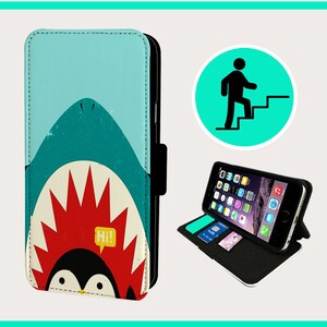 May include: A teal and white phone case featuring a cartoon shark design with a penguin. The case is open, displaying a smartphone with a screen showing app icons. The case has slots for cards. A green circle with a person climbing stairs is also shown.