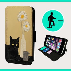 Pode incluir: Um gato preto com olhos amarelos sentado em uma mesa com um vaso de flores brancas e uma caneca branca. A imagem é impressa em uma capa de telefone de couro marrom.
