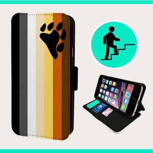 Puede incluir: Una funda de teléfono negra con un diseño de rayas multicolores y una huella de pata negra. La funda está abierta para revelar un teléfono negro con una pantalla que muestra iconos. La funda tiene una función de soporte y una ranura para tarjetas.