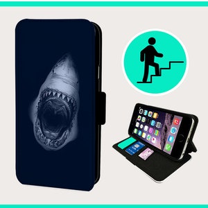 May include: A blue phone case with a white shark graphic. The shark's mouth is open and its teeth are visible. The case is designed to fit a smartphone.