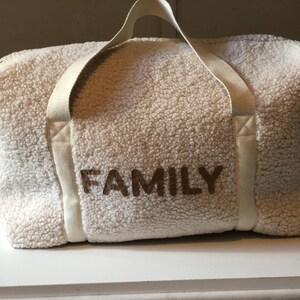 May include: White faux fur duffel bag with brown embroidered text that reads "FAMILY".