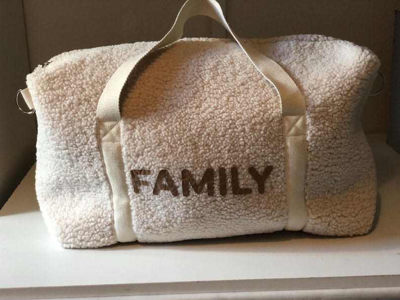 May include: White faux fur duffel bag with brown embroidered text that reads "FAMILY".