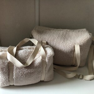 May include: Two white fluffy sherpa bags with cream colored straps. The smaller bag has two top handles and the larger bag has a single top handle and a long strap.