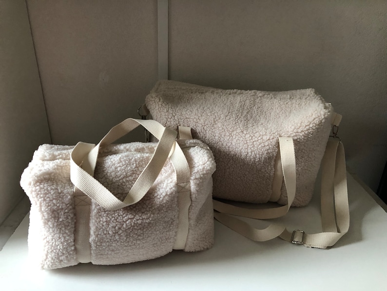 May include: Two white fluffy sherpa bags with cream colored straps. The smaller bag has two top handles and the larger bag has a single top handle and a long strap.