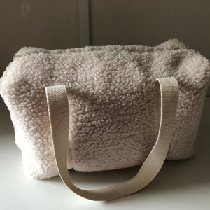May include: A white fluffy tote bag with two long straps. The bag is made of a soft, fuzzy material.