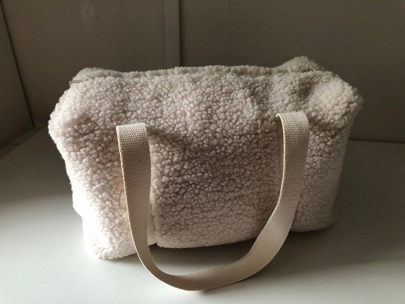 May include: A white fluffy tote bag with two long straps. The bag is made of a soft, fuzzy material.