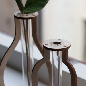 May include: Two wooden vases with clear glass tubes for holding flowers. The vases are made of light brown wood and have a simple, modern design.