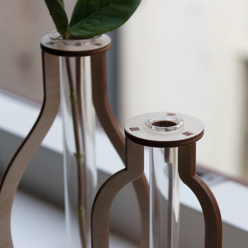 May include: Two wooden vases with clear glass tubes for holding flowers. The vases are made of light brown wood and have a simple, modern design.