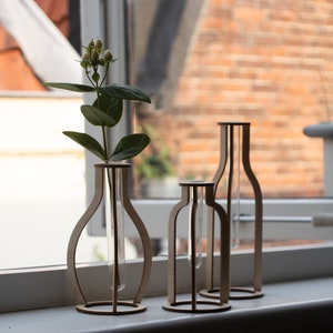 May include: Three wooden vases with glass test tubes inside. The vases are different sizes and shapes. The vase on the left has a small bouquet of white flowers.
