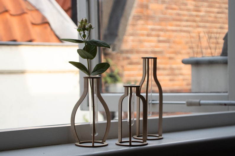May include: Three wooden vases with glass test tubes inside. The vases are different sizes and shapes. The vase on the left has a small bouquet of white flowers.