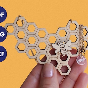 May include: A wooden honeycomb pendant necklace with a small wooden bee charm and a clear acrylic charm with the word "deep" on it. The necklace is on a gold chain.