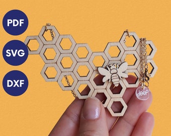 May include: A wooden honeycomb pendant necklace with a small wooden bee charm and a clear acrylic charm with the word "deep" on it. The necklace is on a gold chain.