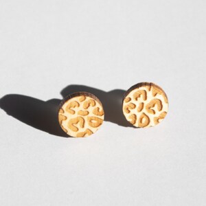 May include: A pair of wooden earrings with a leopard print design. The earrings are round and have a light brown color.