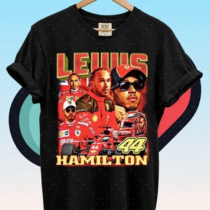 Pode incluir: Camiseta preta com um gr&aacute;fico em estilo vintage de Lewis Hamilton com fato e capacete de corrida vermelhos. O design inclui os textos "LEWIS" e "HAMILTON" e o n&uacute;mero "44".