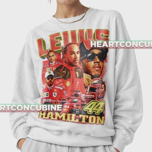 Pode incluir: Camisola branca com um gr&aacute;fico de Lewis Hamilton em v&aacute;rias poses, um carro de corrida e um capacete. O texto "LEWIS HAMILTON 44" &eacute; em vermelho e amarelo.