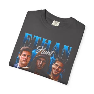 Graphite washed Comfort Colors graphic t-shirt with Ethan Hunt action hero collage print, retro espionage-inspired artwork, unisex oversized tee, dark movie fan streetwear style.