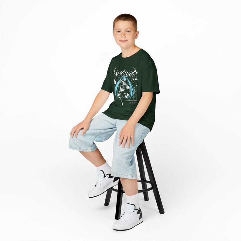 May include: Dark green t-shirt featuring a graphic of a female anime character with blue hair and the text "Lingua Ignota". The shirt is worn with light blue denim shorts and white sneakers. The person is sitting on a black stool.