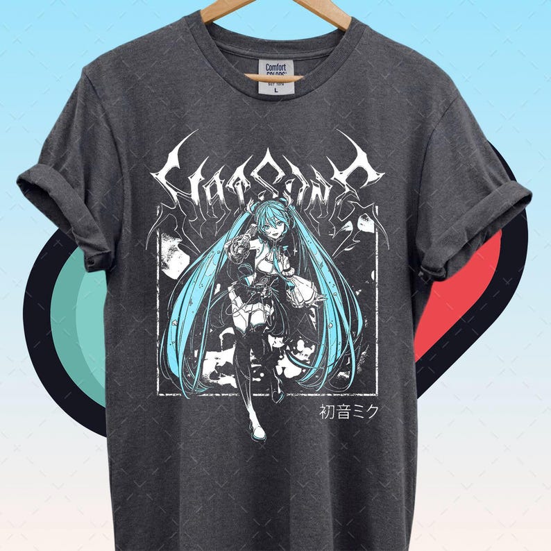 May include: Dark gray t-shirt featuring a graphic of a female anime character with long turquoise hair. The design includes the text "Hatsune Miku" in a stylized font and Japanese characters. The shirt is made of a soft material.