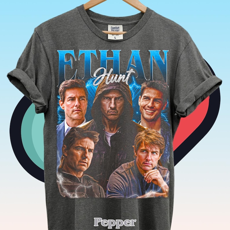 Może przedstawiać: Ciemnoszary t-shirt z kr&oacute;tkim rękawem z nadrukiem graficznym przedstawiającym postać Ethana Hunta w r&oacute;żnych pozach. Projekt zawiera napis "ETHAN" dużymi niebieskimi literami, "Hunt" białą kursywą oraz "Pepper" w kolorze białym na dole.