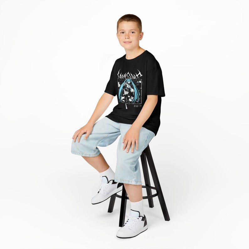 May include: Black t-shirt featuring a graphic design with a blue-haired anime character and Japanese text. The shirt is worn with light blue denim shorts and white sneakers. The person is sitting on a black stool against a white background.