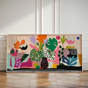 May include: A framed art print with a colourful, abstract floral design. The artwork features a variety of flowers and leaves in shades of orange, pink, green, and black, set against a light pink backdrop. The print is in a white frame.