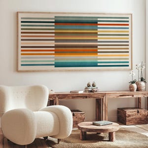 Puede incluir: Una gran obra de arte enmarcada con rayas horizontales en tonos de naranja, azul, verde y marrón cuelga sobre una consola de madera. Una butaca blanca y curvada se encuentra frente a la consola. Una mesa de centro redonda de madera y una alfombra tejida están en primer plano.