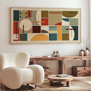 Puede incluir: Un cuadro enmarcado con un diseño Bauhaus que presenta formas geométricas en varios colores, como rojo, azul y amarillo. La impresión tiene la palabra "BAUHAUS" a la izquierda y "WEIMAR 1919" en la parte superior derecha. Se muestra sobre una consola de madera.