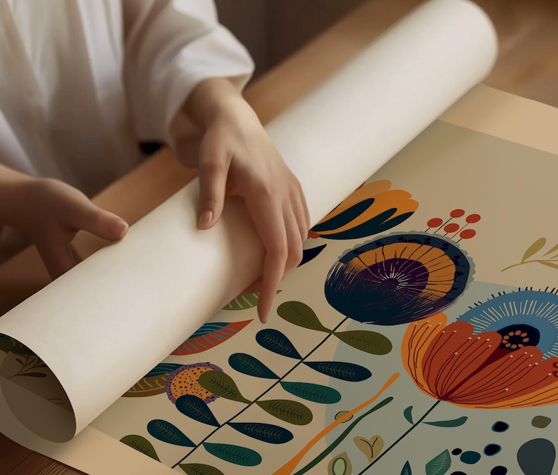 May include: A rolled-up art print with a floral design is being unrolled. The print features large, stylized flowers in shades of orange, blue, and purple, with green leaves and stems against a light background. The print is being unrolled on a wooden surface.