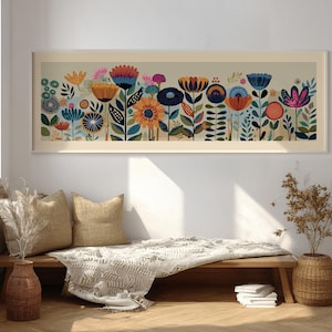 May include: A framed floral art print featuring a colorful array of stylized flowers in shades of orange, blue, pink, and yellow. The artwork is set against a neutral background and framed in a light-colored wood. The print is displayed above a wooden bench with pillows and a blanket.