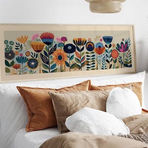 May include: A framed floral art print featuring a colorful array of stylized flowers in shades of blue, orange, pink, and yellow. The artwork is set against a light beige background and framed in a light wood tone. The print is displayed above a bed with pillows.