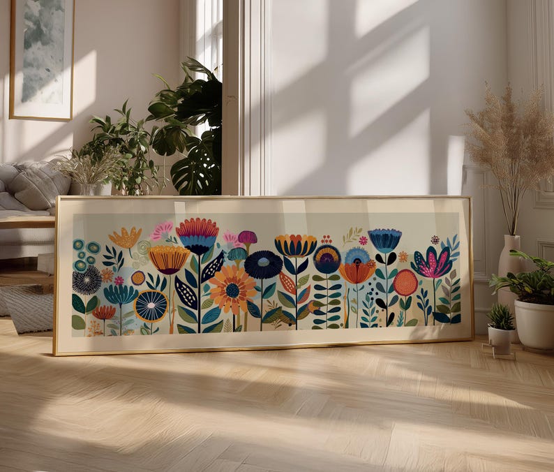 May include: A framed floral art print featuring a colorful array of stylized flowers in shades of blue, orange, pink, and green. The artwork is set against a light background and framed in a gold-colored frame. The print is displayed on a wooden floor.