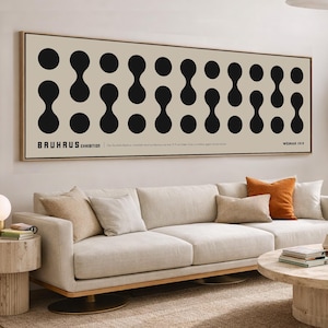 Könnte beinhalten: Ein gerahmtes Bauhaus-Ausstellungsposter mit einem sich wiederholenden Muster aus schwarzen Formen auf beigem Hintergrund. Das Poster hängt über einem hellen Sofa mit orangefarbenen und beigen Kissen. Der Raum hat eine moderne, minimalistische Ästhetik.