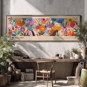 Puede incluir: Una impresión artística enmarcada con un diseño floral vibrante, que presenta varias flores coloridas. La impresión incluye el texto "YAYOI KUSAMA" y texto japonés. La obra de arte se exhibe en una habitación con un escritorio de madera, una silla y plantas.