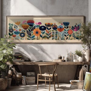 May include: A framed floral art print featuring a colorful array of stylized flowers in shades of orange, blue, pink, and yellow. The artwork is set against a neutral background and framed in a light wood. The print is displayed in a well-lit room with plants and a wooden desk.
