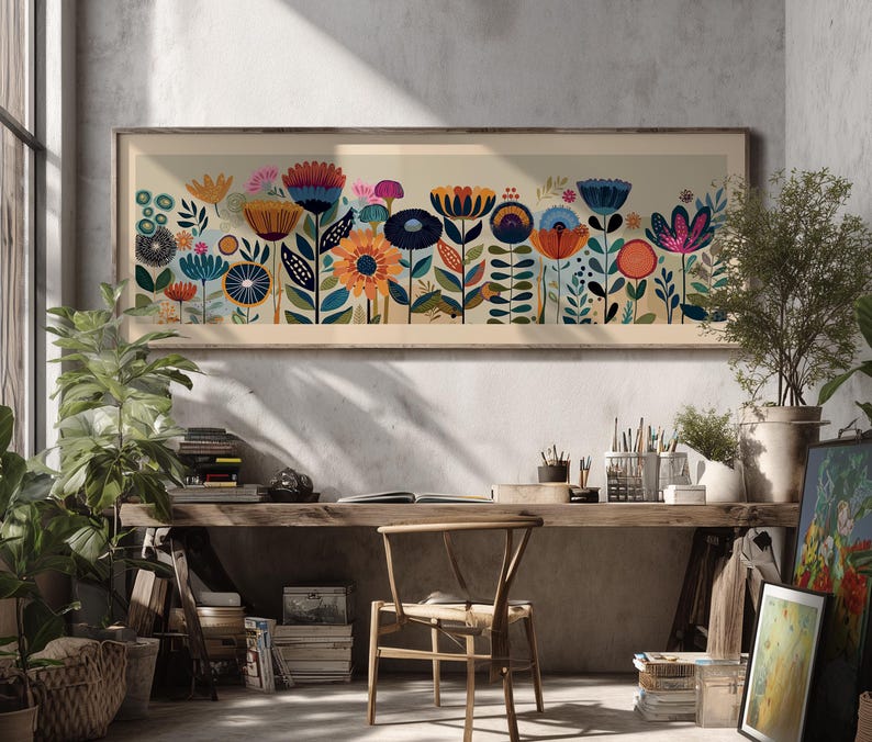 May include: A framed floral art print featuring a colorful array of stylized flowers in shades of orange, blue, pink, and yellow. The artwork is set against a neutral background and framed in a light wood. The print is displayed in a well-lit room with plants and a wooden desk.
