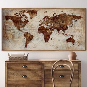 May include: A framed world map with a vintage aesthetic. The map features a sepia-toned colour palette with brown continents and a cream-coloured background. The map is displayed above a wooden dresser.