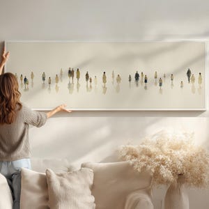 Könnte beinhalten: Ein langer, rechteckiger Kunstdruck mit Miniaturfiguren in verschiedenen Outfits. Das Kunstwerk ist überwiegend beige und weiß, wobei die Figuren zu gehen scheinen. Der Rahmen ist weiß, und das Kunstwerk wird von einer Person gehalten.