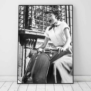 Puede incluir: Fotografía en blanco y negro de una mujer conduciendo una scooter. Lleva una camisa blanca y una bufanda oscura. Sonríe y mira hacia la derecha. La scooter está en primer plano y la mujer está en el fondo.