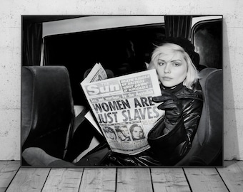 May include: Black and white photograph of a person holding a newspaper with the headline "WOMEN ARE JUST SLAVES." The person is wearing a black hat, jacket, and gloves. The newspaper is open, and the person is looking at the camera.