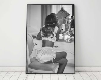 Può includere: Una fotografia in bianco e nero di una persona seduta davanti a uno specchio da toeletta, con un completo di lingerie in raso bianco. La persona sta guardando il suo riflesso nello specchio.