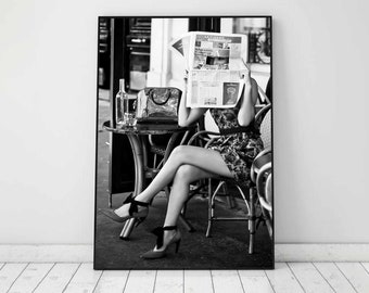 May include: Black and white photo of a person sitting at a cafe table, reading a newspaper with the headline "Le Journal Economie". The person is wearing a floral dress and black heels.