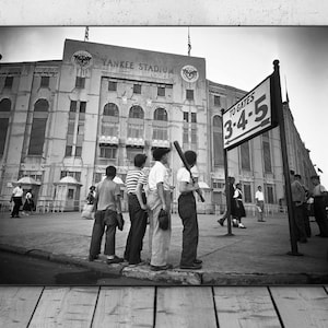 May include: Black and white photograph of Yankee Stadium with a group of boys holding baseball bats and gloves. A sign reads "TO GATES 3-4-5". The image captures a moment in time, likely from the mid-20th century.