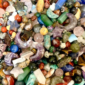 May include: A selection of polished gemstones in diverse shapes and colours. The collection features stars, moons, spheres, and pointed crystals in shades of green, blue, purple, red, and brown. The gemstones vary in size and texture.