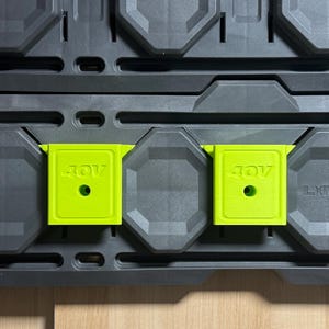 May include: A close-up shot of a gray storage system with two bright green 40V battery holders. The holders are square with a circular hole and the text "40V". The storage system has a grid-like design.