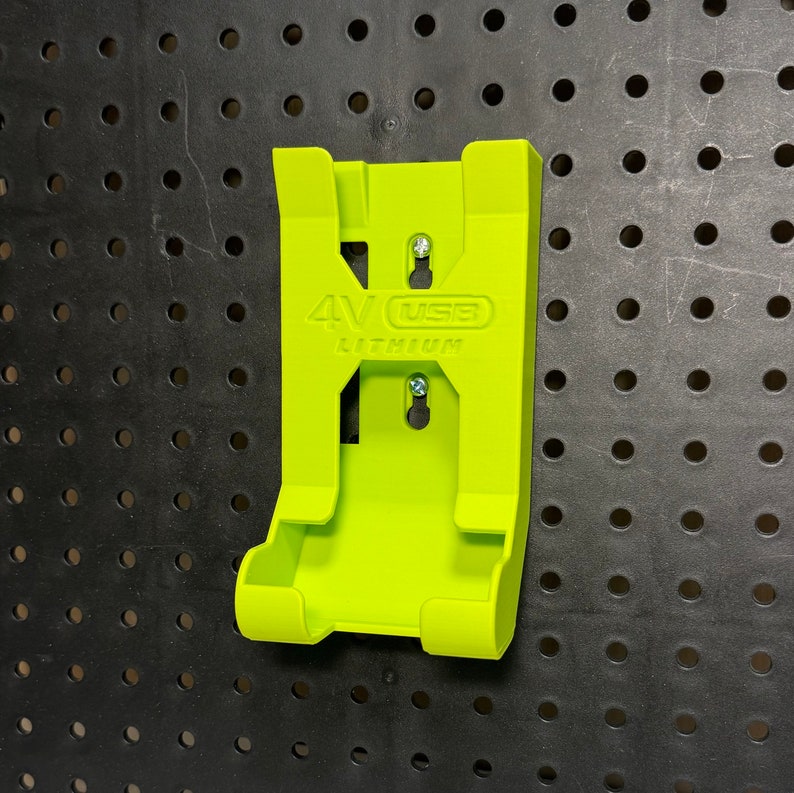 Puede incluir: Un soporte de pared verde lima para una bater&iacute;a de litio USB de 4V. El soporte tiene dos ranuras para la bater&iacute;a y un agujero para colgar.