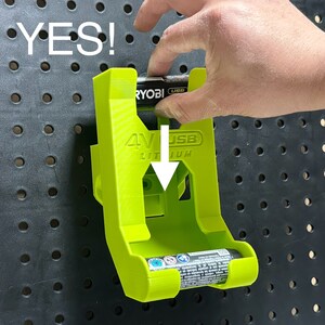 Puede incluir: Un soporte de pared verde brillante para guardar una bater&iacute;a Ryobi 4V USB Lithium. El soporte tiene una ranura para la bater&iacute;a y una etiqueta que dice "4V USB Lithium".