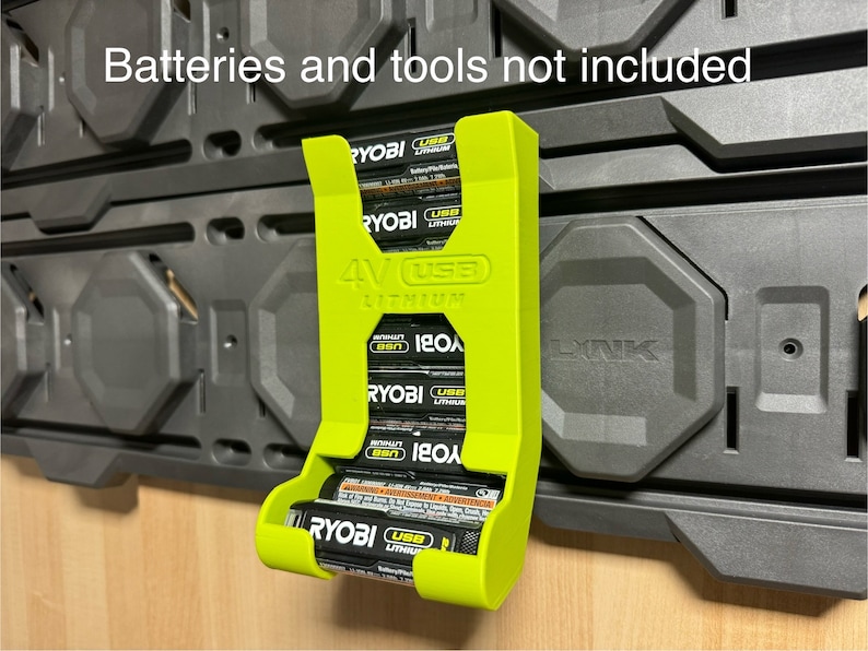 Puede incluir: Un soporte de bater&iacute;a impreso en 3D de color verde para bater&iacute;as de litio Ryobi de 4V. El soporte est&aacute; montado en una pared negra y tiene capacidad para cuatro bater&iacute;as. El texto "Batteries and tools not included" es visible en la parte superior de la imagen.