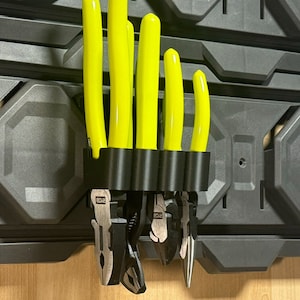 May include: A black tool holder with five slots for holding pliers. The holder is mounted on a gray wall. The pliers are yellow and have black handles. The text "Tools are not included" is printed on a green label below the holder.